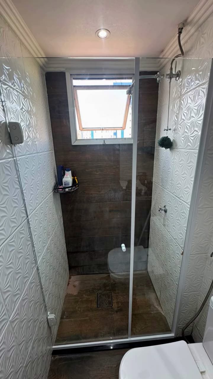 Banheiro depois: box de vidro temperado instalado, com porta de abrir e perfis brancos.